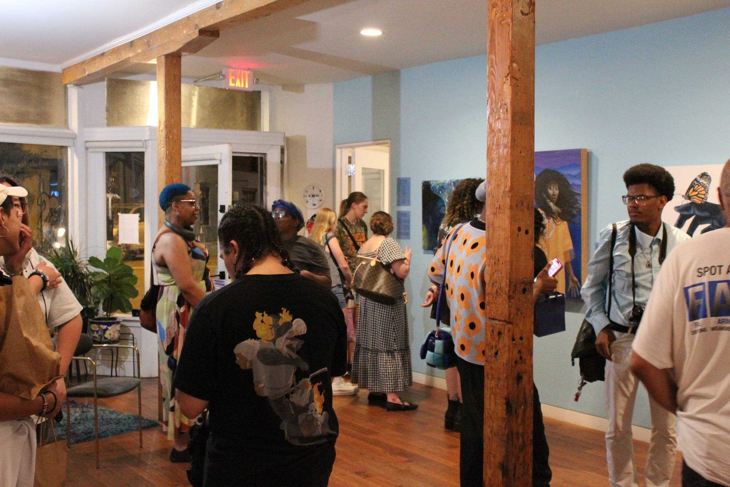 A crowded gallery with blue walls and wooden posts, visitors gathered in front of paintings