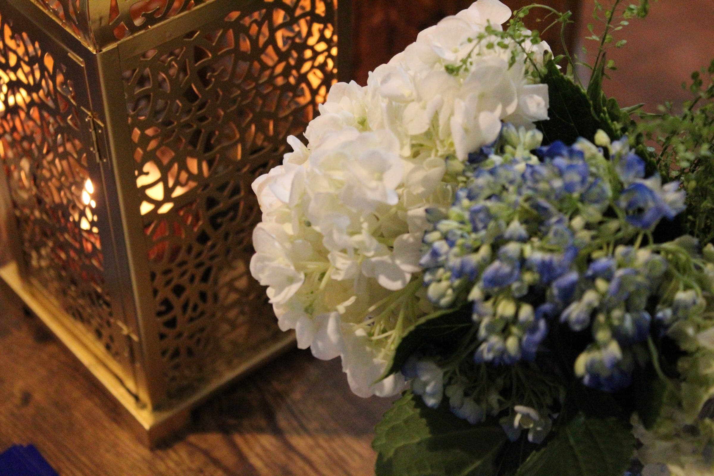 A pierced brass lantern glows beside a bouquet of white and blue hydrangeas